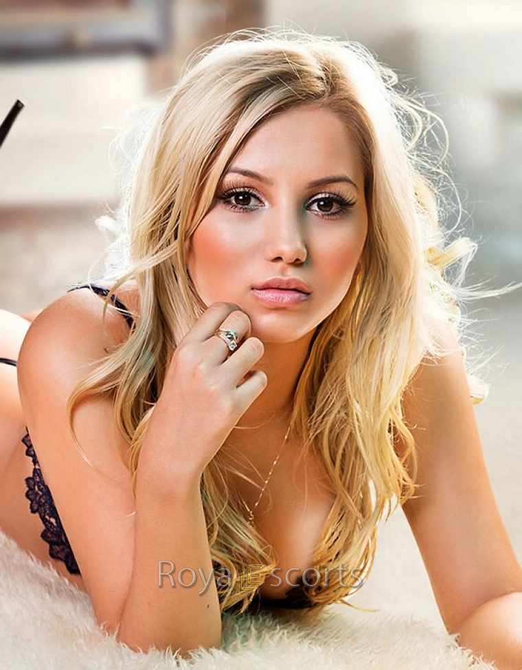 sexy blonde female escort showing her cleavage while resting on her elbow